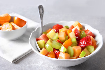 Bowl with fresh fruit salad on grey background