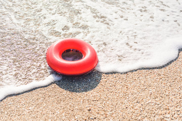 Inflatable red donut on a foam soft sea waves at seashell beach. Sunny summer vacation day with family.