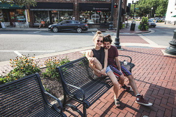 happy young hipp couple sitting on a bench on the sidewalk