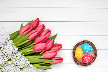 Decorative Easter eggs in nest and red tulips on white wooden table. Copy space, top view. Easter background.