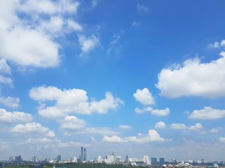 White puffy cumulus clouds computing over cityscape of Johor Bahru, Malaysia with clear blue skies