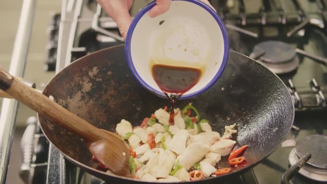 Man Pouring Soya Sauce Over Chicken And Peppers In Wok