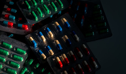 Pile of colorful capsule pills in blister pack on dark background. Drug policy and budgets....