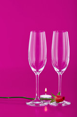 Two wine glasses with rose and candle on pink background