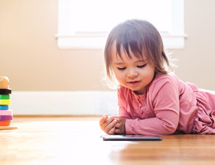 Happy toddler girl playing with her tablet computer in her house