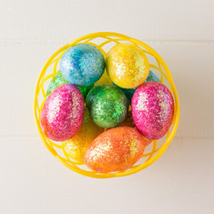 Basket with colorful eggs on a white wooden table. The view from the top.
