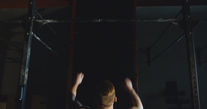 Back view of unrecognizable tattooed sportsman without shirt doing chin-ups hanging on bar in sunny gym. Slow motion 4K shot on Red cinema camera.