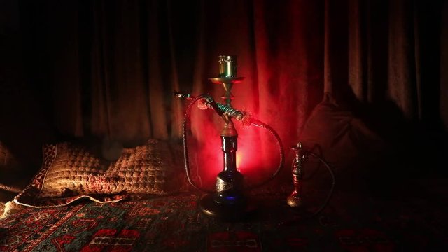 Hookah hot coals on shisha bowl making clouds of steam at Arabian interior. Oriental ornament on the carpet. Stylish oriental shisha in dark with backlight. Shisha on rotating display. Slider shot