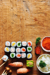 Assorted sushi with omelette, shrimp, salmon, caviar and wakame, bowl of rice, tobiko on wooden table. Flat lay with space for text.