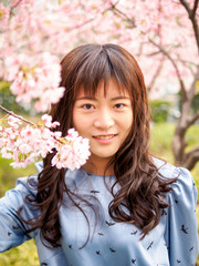 Fototapeta premium Outdoor portrait of beautiful young Chinese girl in blue dress smiling among blossom cherry tree brunch in spring garden, beauty, summer, emotion, expression and people concept.