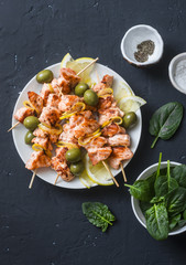 Salmon skewers, olives, spinach - snack, appetizers, tapas. Grilled salmon fish skewer on a dark background, top view