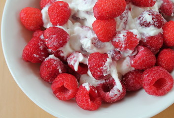 Raspberries mixed with yogurt in white bowl.