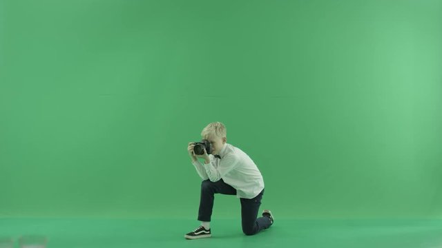 Squatting boy is taking photos of the left side in the centre of the green screen
