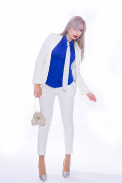 Studio portrait in full length of a beautiful young blond woman with long hair in a white pants suit. A girl in silvery shoes with high heels, in her hands she holds a small silver handbag