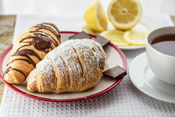 Fresh baked croissants with chocolate for breakfast, a cup of tea, lemon