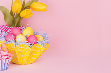 Easter spring home decor of yellow tulips, painted eggs, cupcake on pastel soft pink background.