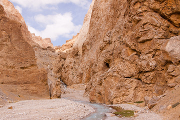 View of blue water source in canyon with textured yellow rocks, tiny green meadow and blue sky background. Region Ladakh. State Jammu and Kashmir, India.