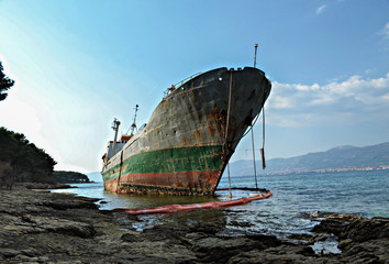 An old ruined ship sits rusting on the shore.