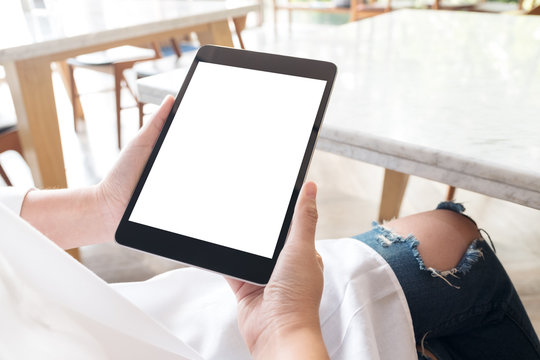 Mockup image of a woman sitting cross legged and holding black tablet pc with blank white desktop screen in cafe