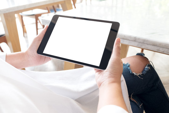 Mockup image of a woman sitting cross legged and holding black tablet pc with blank white desktop screen in cafe