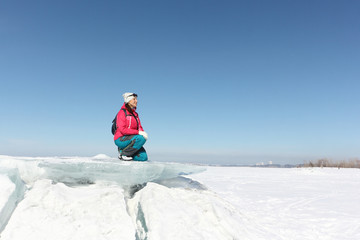 Fototapeta na wymiar Happy woman in a red jacket sitting on an ice floe on a frozen river, Ob reservoir, Russia