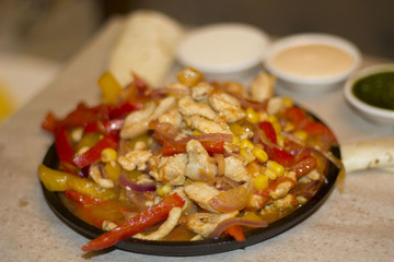 pieces of meat with onion pepper corn on a frying pan and sauces on the table