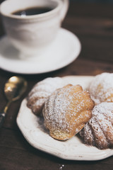 Homemade french madeleines with beurre noisette and cup of coffee on wooden table. Vertical.
