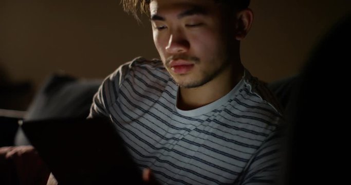 4K Young man relaxing at home with digital tablet, surfing the web late at night