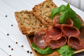 Salami smoked sausage slices basil leaves and peppercorns on white background