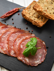 Salami smoked sausage slices basil leaves and peppercorns on black stone background