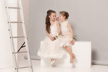 Little pretty girls with flowers dressed in wedding dresses