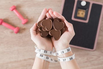 Woman's tied hands with a measuring tape and chocolate hearts. New start for healthy nutrition, body slimming, weight loss. Cares about body. Prohibited desires, temptation of sweets during the diet.
