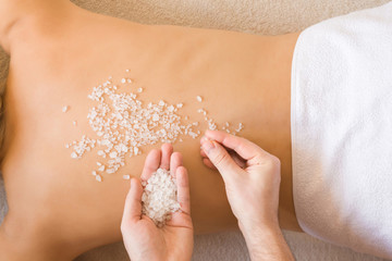 Beautiful woman lying and getting white sea salt scrub treatment in health spa. Masseur hands doing massage on young calm woman's back in beauty salon. Enjoying life. Relaxing day. Body care concept.
