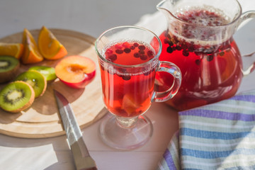 Compote of red berries in a pitcher and a glass, fresh fruit on a rustic table