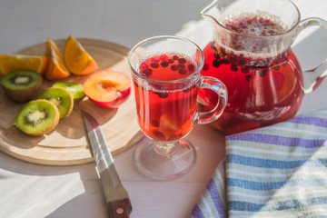 Compote of red berries in a pitcher and a glass, fresh fruit on a rustic table