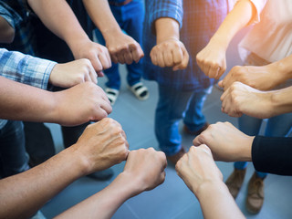 Closeup image of many people putting their fists together as symbol of unity with sunlight effect.