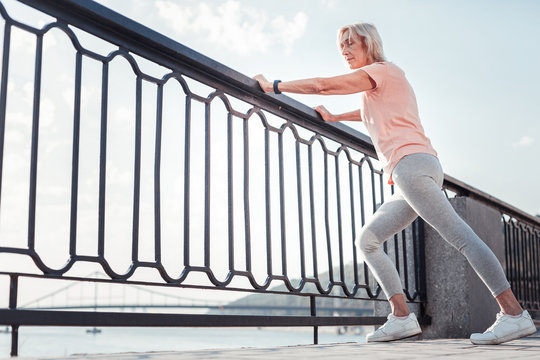 Exercise and training. Thoughtful athletic confident woman standing on the quay warming up relying on the railing.