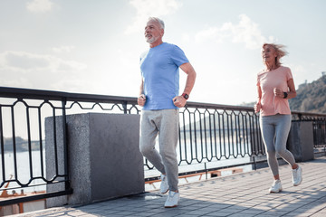 Healthy is the most important. Joyful aged confident man running across the quay with a woman...