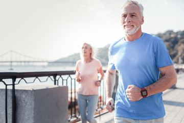 Life is good. Satisfied athletic unshaken man spending time on fresh air looking straight and having cardio exercises on the quay.