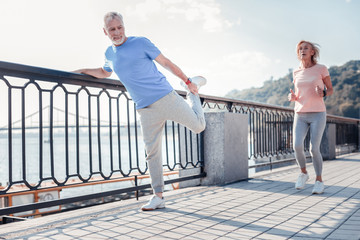 Sport for everyone. Satisfied unshaken senior man spending time on fresh air holding by the railing...