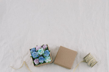 Brown gift box and rope decorate with blue tone paper flowers on muslin fabric with copy space, selective focus on flowers in box