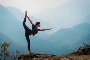 Poster Young woman practices yoga on mountain cliff at sunrise. Mountanious landscape © zulman