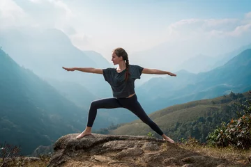 Fotobehang Woman doing yoga on mountain cliff at sunrise. Mountanious landscape © zulman