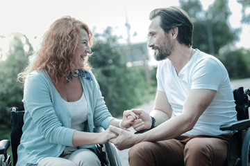 My support. Cheerful invalid female sitting on her wheelchair near her man and expressing...