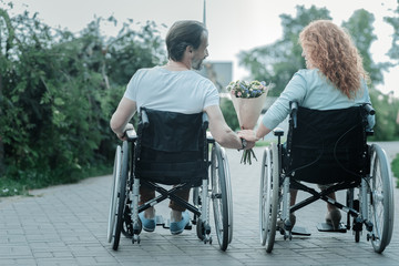 Warm atmosphere. Relaxed woman sitting in wheelchair and taking flowers while looking at her boyfriend