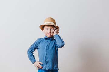 little boy in blue shirt in hat talking on phone on white background