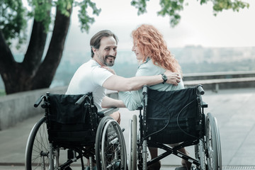 Look at us. Attractive invalid man keeping smile on his face and embracing his woman while being...