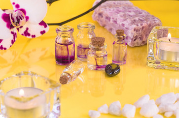 Miniature glass bottles for aroma oils. Overhead shot of orchid flower, glass candle holders, lavender soap and Spa salt lie on a yellow background. Nature concept.