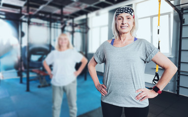Fototapeta na wymiar Get up and move. Hazel eyed elderly lady posing into the camera with her hands on the hips while standing in a gym and taking a group exercise class.