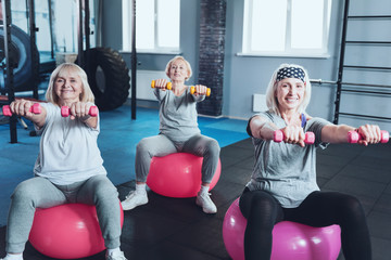 Train with us. Selective focus on two sporty senior women sitting on fitness balls and working with dumbbells while taking a group exercise class.